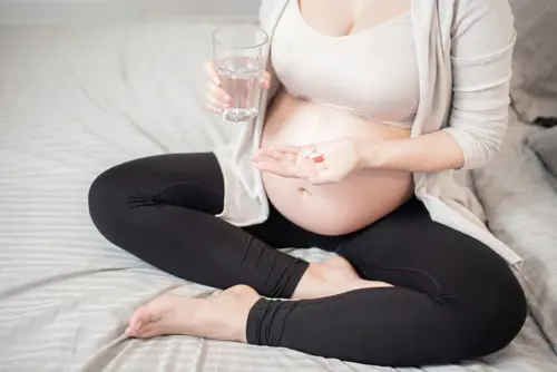 Grūtniece sēž uz gultas un lieto ikdienas vitamīnu devu.